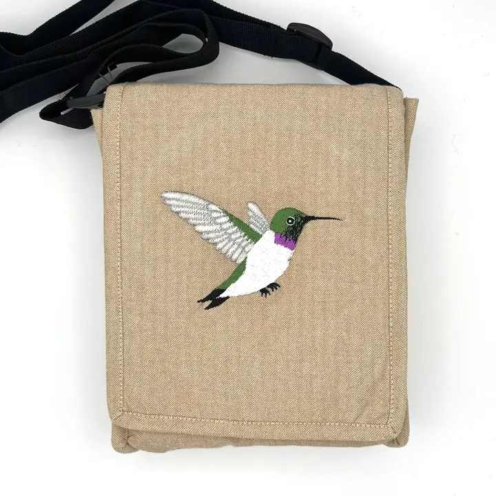 Beige canvas crossbody bag with an embroidered green-and-purple hummingbird on the front.